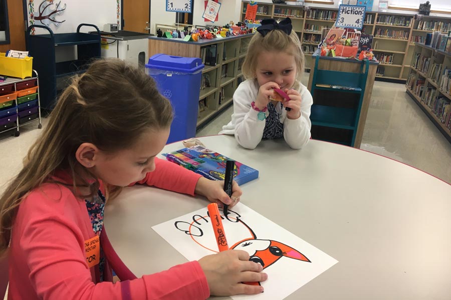 two girls coloring pictures at table in classroom