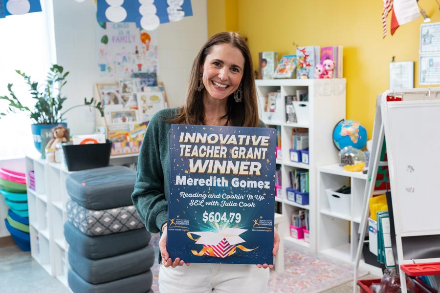 teacher in classroom smiling and holding Grant Winner sign